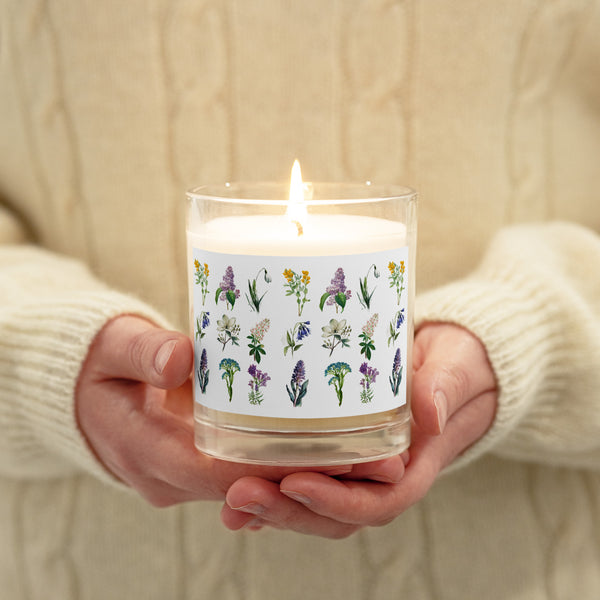 A person holding a glass jar soy wax candle with Spring flowers design all around.