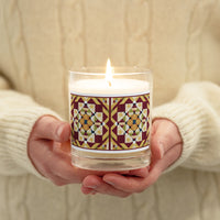 A person holding a sleek glass jar soy candle with a country farmhouse barn quilted pattern design of Autumn Season color scheme. 